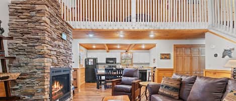 A spacious living area with a stone fireplace, a wooden ceiling, and a balcony.