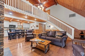 A spacious living area with a wooden floor, a leather sofa, a coffee table, and a staircase with a white railing.