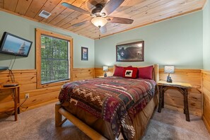 A bedroom with a bed, a ceiling fan, a television, a window with blinds, and a painting on the wall.