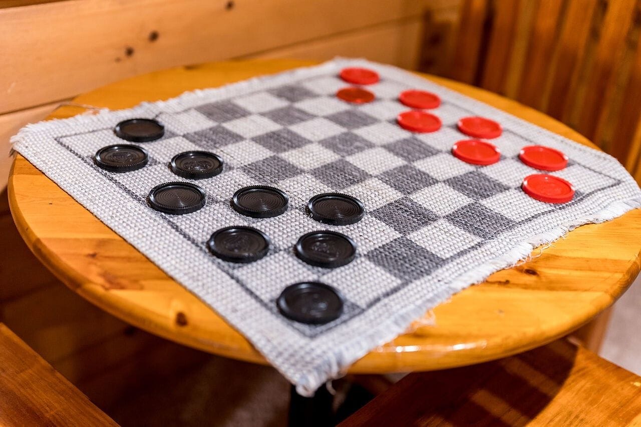 A checkered board game with black and red pieces on a round wooden table.