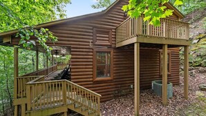 Eine zweistöckige Blockhütte mit Balkon, überdachter Veranda und einer Treppe, die zum oberen Stockwerk führt.