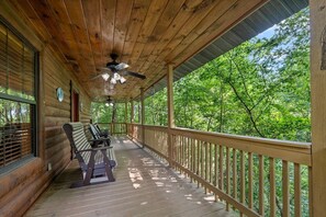 Eine Holzveranda mit Deckenventilator, einer Sitzbank und Blick auf einen Wald.