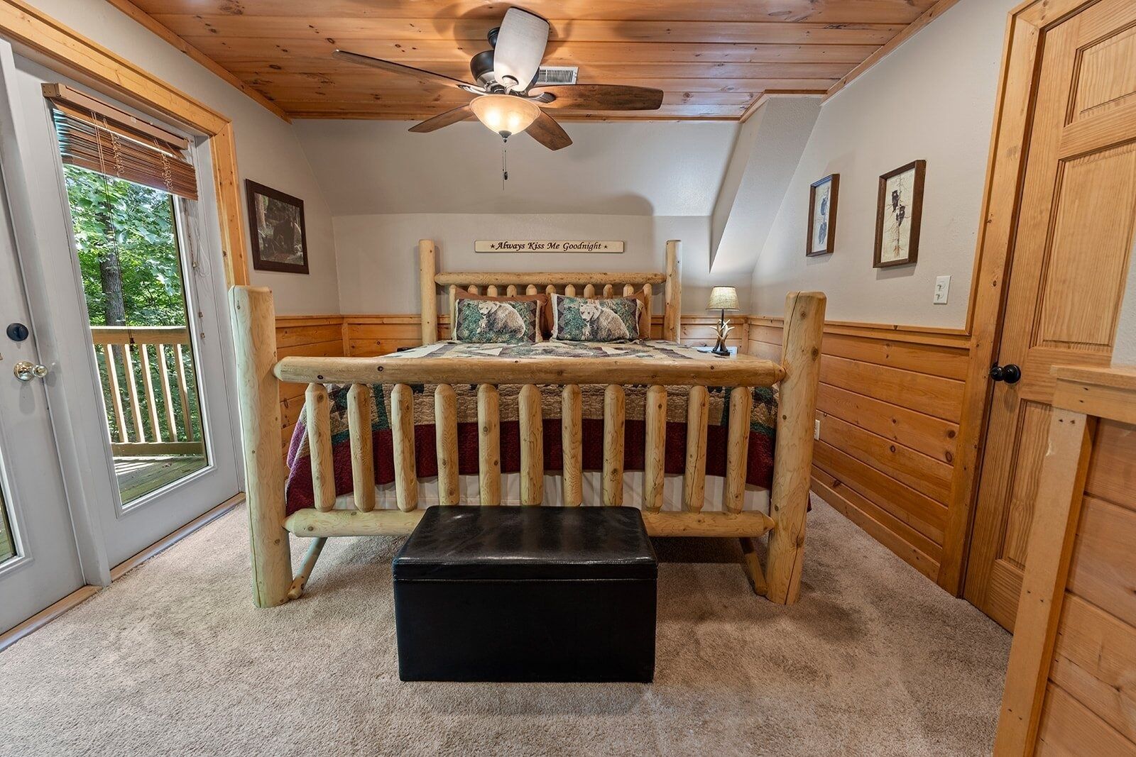 Un dormitorio con una cama de madera, un ventilador de techo, un banco y una puerta que da a un balcón.