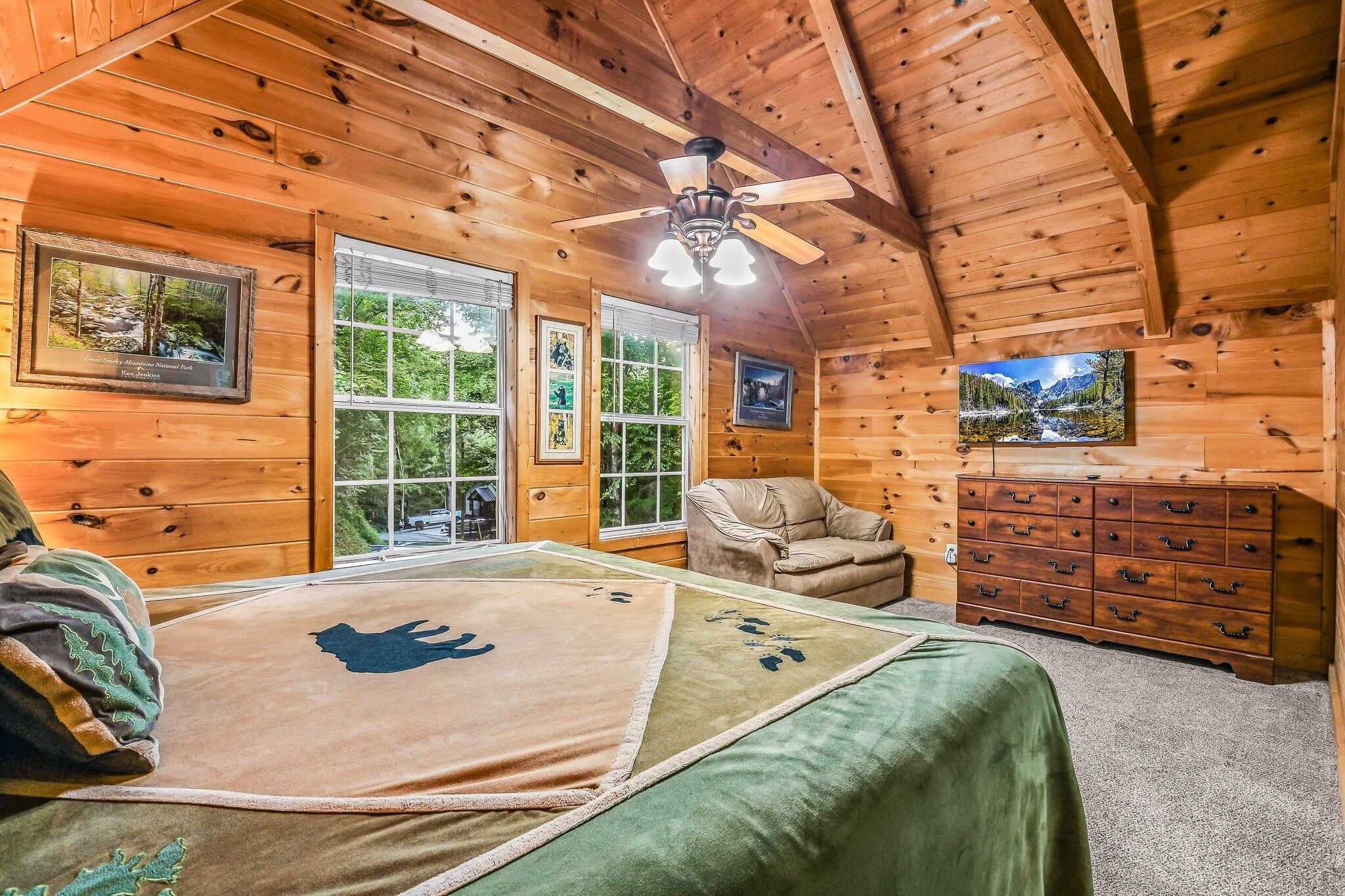 A wooden cabin bedroom with a bed, a chair, a dresser, and framed pictures on the walls.