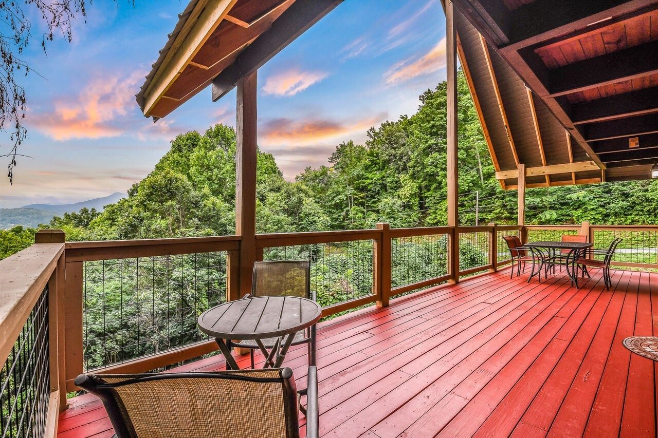 A wooden deck with a table and chairs, overlooking a forested area.