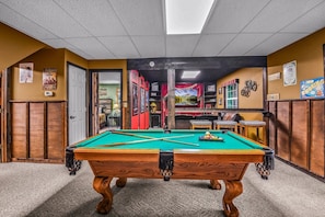 A pool table in a room with wooden paneling, a door, and a wall with various signs and decorations. - Bearly Hidden Ridge 5 Bedroom Cabin by RedAwning (Gatlinburg)