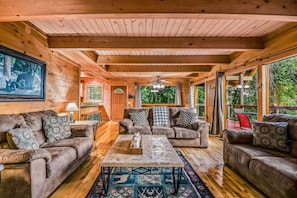 A cozy cabin interior with wooden walls, a fireplace, and a large window overlooking greenery. - Bearly Hidden Ridge 5 Bedroom Cabin by RedAwning (Gatlinburg)