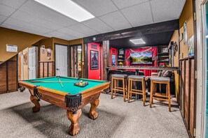 A pool table with a green felt surface, surrounded by wooden stools and a red wall with movie posters. - Bearly Hidden Ridge 5 Bedroom Cabin by RedAwning (Gatlinburg)