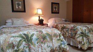 Habitación de hotel con dos camas, cada una con ropa de cama floral, una mesita de noche con lámpara y cuadros en la pared.