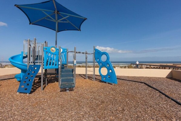 A playground with a blue slide, climbing structures, and a shaded area.