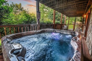 A hot tub with a wooden deck and stone walls, surrounded by lush greenery. - The Ranch Cabin on 6 Secluded Acres in the Great Smoky Mountains by RedAwning (Sevierville)