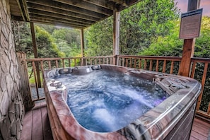 A hot tub on a wooden deck with a safety sign, surrounded by lush greenery. - The Ranch Cabin on 6 Secluded Acres in the Great Smoky Mountains by RedAwning (Sevierville)
