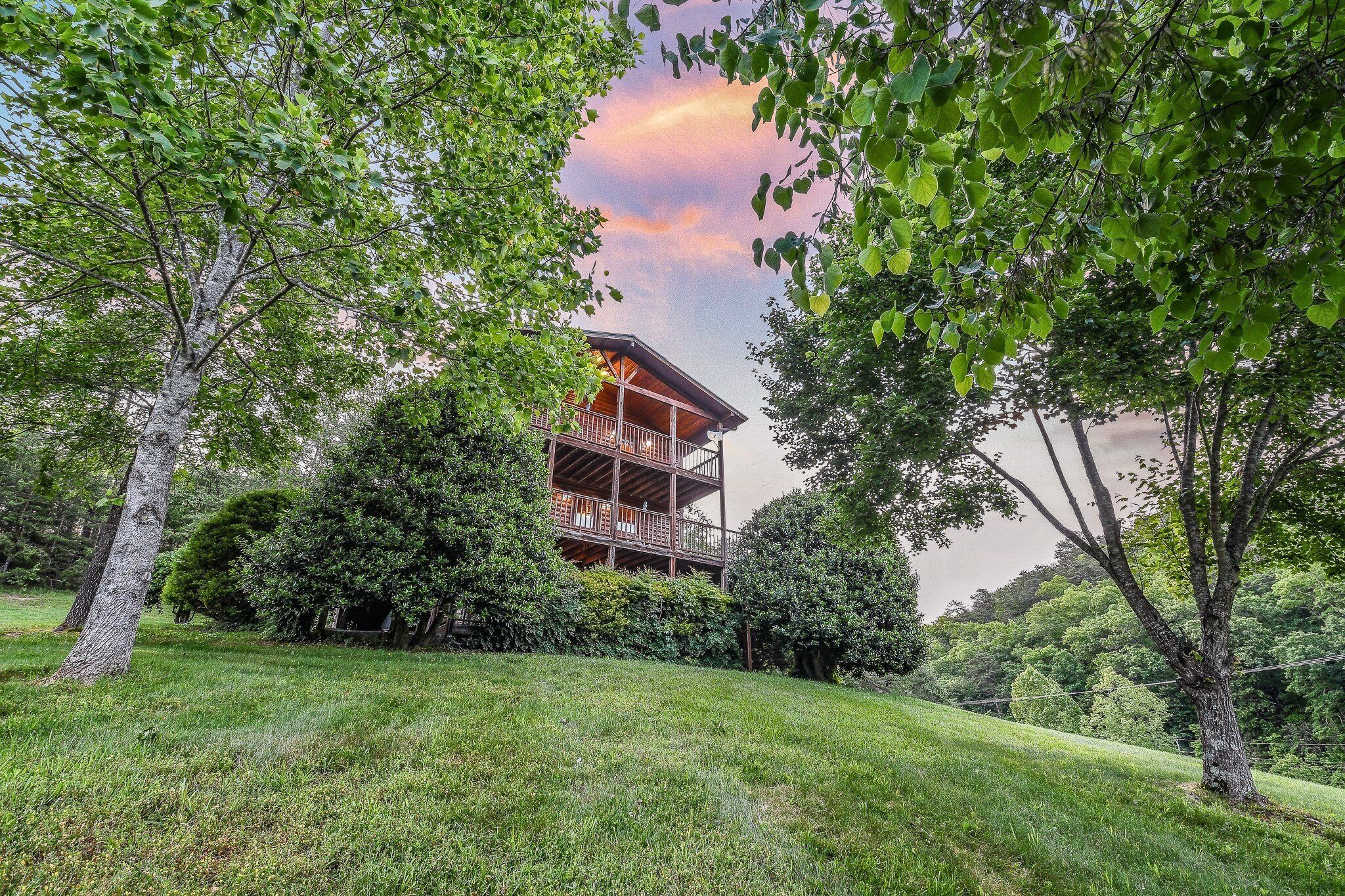 A two-story wooden building with a balcony, surrounded by lush greenery and trees.