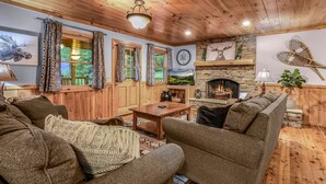 A cozy living room with wooden walls and ceiling, a stone fireplace, a television, and comfortable seating. - The Ranch Cabin on 6 Secluded Acres in the Great Smoky Mountains by RedAwning (Sevierville)