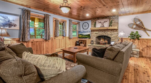 A cozy living room with wooden walls and ceiling, a stone fireplace, a television, and comfortable seating. - The Ranch Cabin on 6 Secluded Acres in the Great Smoky Mountains by RedAwning (Sevierville)