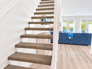 A staircase with carpeted steps leading to a living area with a blue sofa and a view of the outdoors. - Coconut Palms Townhome 2 Bedroom Townhouse by RedAwning (New Smyrna Beach)