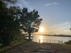 A park with a tree, a fence, and a body of water during sunset. - Coconut Palms Townhome 2 Bedroom Townhouse by RedAwning (New Smyrna Beach)