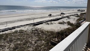 A beach view from a balcony with a sandy path, a wooden fence, and a clear sky.