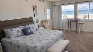 A bedroom with a bed, a bench, a chair, a table, and a view of the beach.