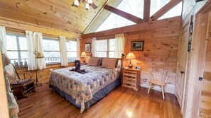 Un dormitori de cabana de fusta amb un llit, dues làmpades de nit, una cadira i una finestra amb cortines.