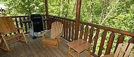 A wooden deck with a grill and two Adirondack chairs.