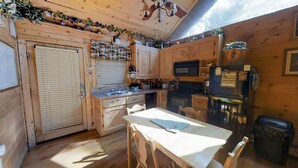 Cocina compacta con armarios de madera, microondas, refrigerador y una mesa de comedor con sillas.