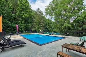 A swimming pool with lounge chairs and a table, surrounded by trees. - Always Kiss Me Goodnight 1 Bedroom Cabin by RedAwning (Sevierville)
