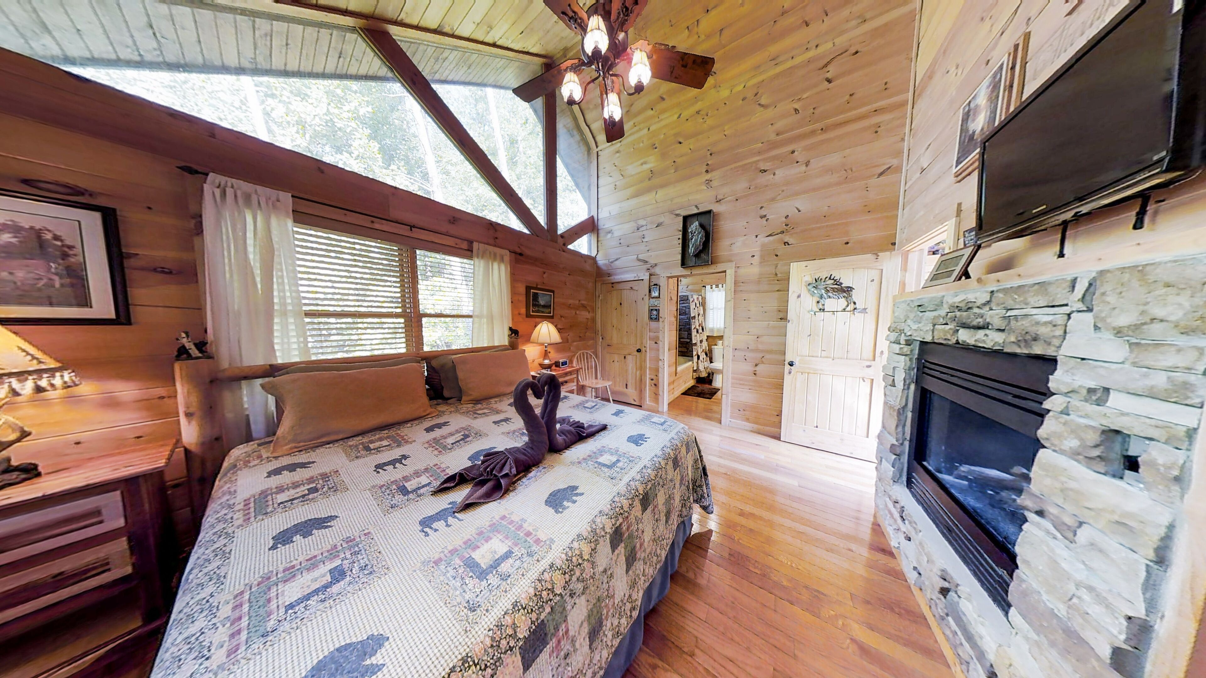 Une chambre confortable dans un chalet, avec un lit, une cheminée, un téléviseur et une fenêtre équipée de stores.