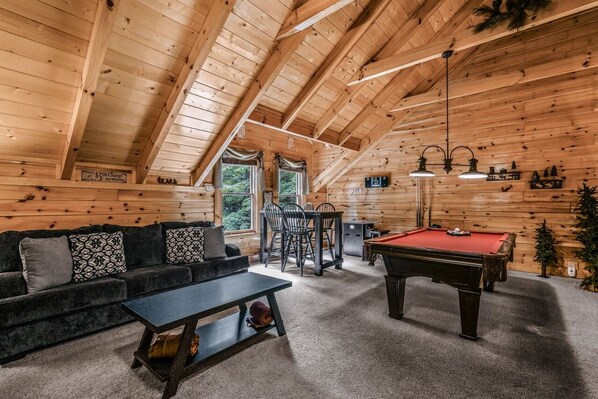 Ein Holzblockhaus-Interieur mit Billardtisch, einer Couch und einem Essbereich.
