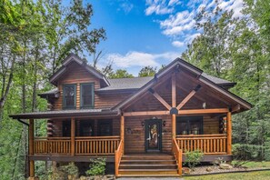 Une cabane en rondins avec une véranda, une porte d’entrée et un petit escalier menant à l’entrée.