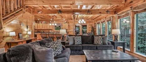 A log cabin interior with a sofa set, dining area, and large windows.