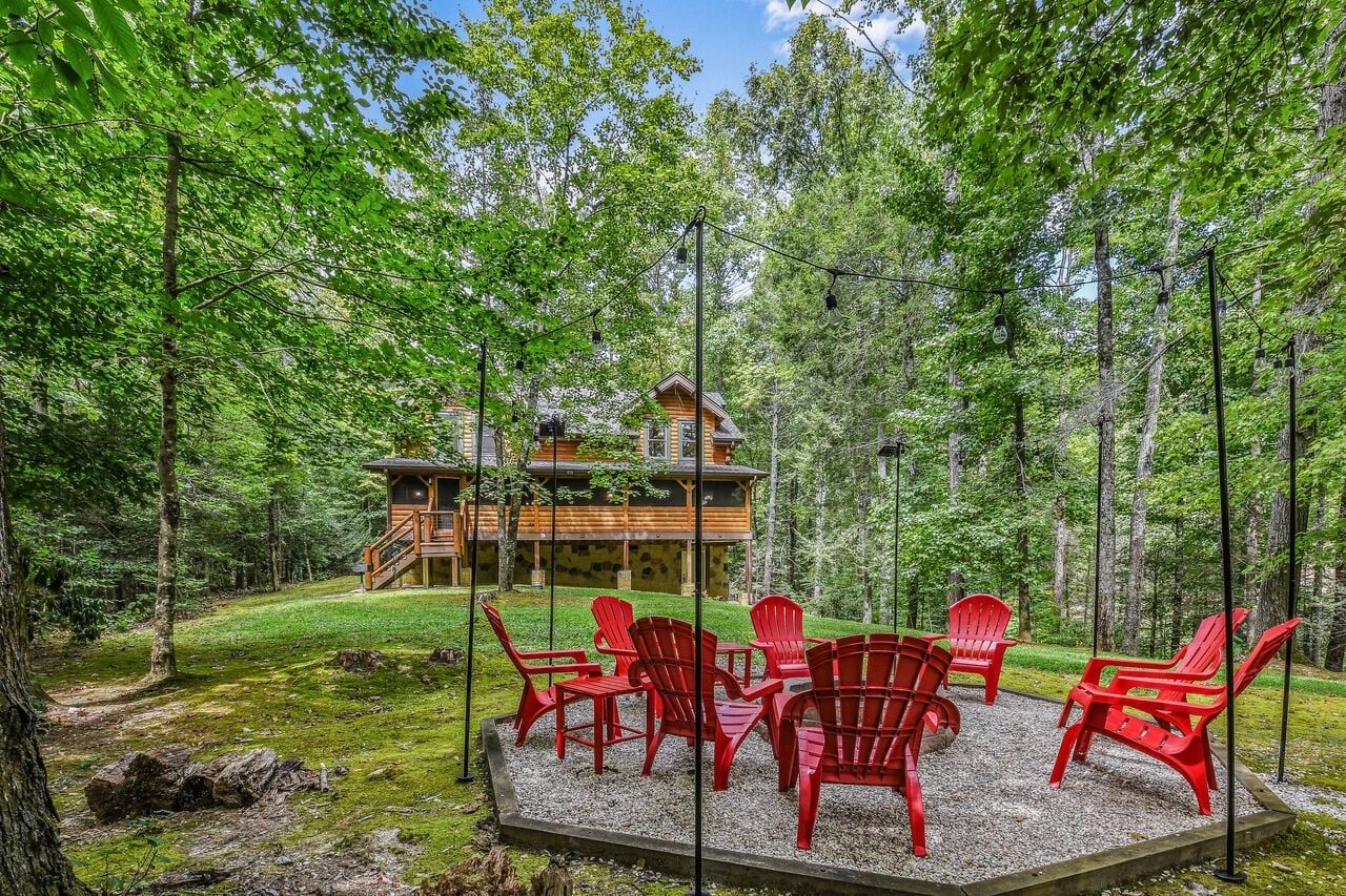 A lodge in a forest with a deck and red chairs.