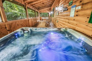 A wooden cabin with a hot tub, wooden walls, and a view of the forest.