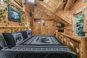 L’intérieur d’un chalet en bois, avec un lit, un ventilateur de plafond et une fenêtre donnant sur l’extérieur.