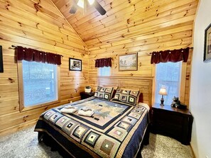 A wooden cabin bedroom with a bed, two windows, a ceiling fan, and a nightstand. - Picture Perfect 2 Bedroom Cabin by RedAwning (Sevierville)