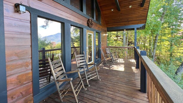 A wooden deck with rocking chairs, large windows, and a view of the surrounding forest. - Picture Perfect 2 Bedroom Cabin by RedAwning (Sevierville)