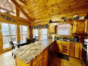 A cabin with a kitchen featuring wooden cabinets, a marble countertop, and a dining area with a table and chairs. - Picture Perfect 2 Bedroom Cabin by RedAwning (Sevierville)