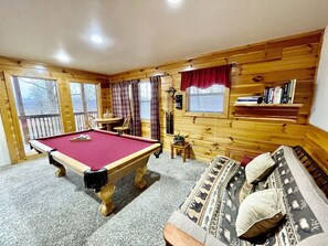 A pool table in a room with wooden walls, a sofa, and a small table with chairs. - Picture Perfect 2 Bedroom Cabin by RedAwning (Sevierville)