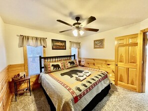 A bedroom with a bed, a ceiling fan, a wooden door, and a window with curtains. - Picture Perfect 2 Bedroom Cabin by RedAwning (Sevierville)