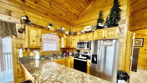 A wooden cabin kitchen with a central island, wooden cabinets, a stainless steel refrigerator, a microwave, and a stove. - Picture Perfect 2 Bedroom Cabin by RedAwning (Sevierville)