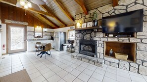 A cozy interior with a stone fireplace, a flat-screen TV, a dining area, and a kitchen with a refrigerator and microwave. - Riverview 1 Bedroom Cabin by RedAwning (Townsend)