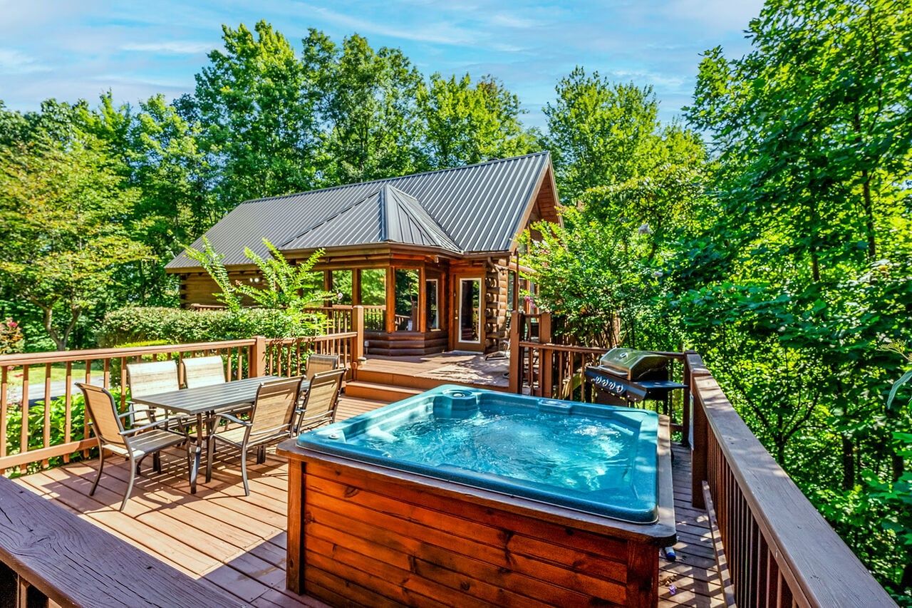 Una terraza de madera con jacuzzi, mobiliario exterior y una zona cubierta con techo metálico.