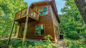 Eine Blockhütte mit Balkon, umgeben von dichtem Wald.