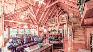 Eine geräumige Holzblockhütte mit hohen Decken, einem gemütlichen Wohnbereich mit Ledersofas, einem Holzesstisch und einer Küchenzeile.