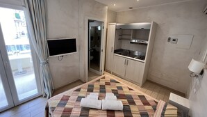A hotel room with a bed, a TV mounted on the wall, a kitchenette, and a bathroom visible through an open door. - Marina Beach Suite Hotel (Rimini)