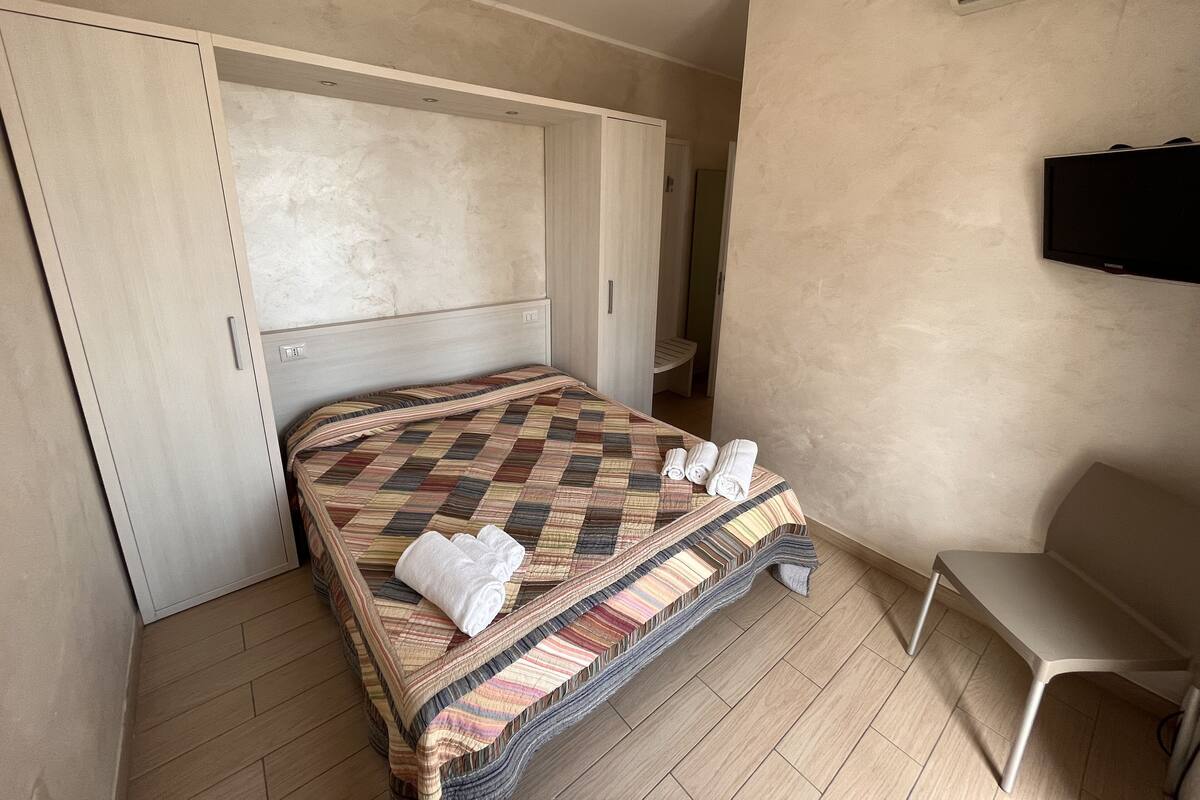A bedroom with a bed, a wardrobe, a chair, and a TV.