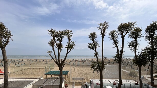 A beachside restaurant with outdoor seating, a view of the beach, and a few trees. - Marina Beach Suite Hotel (Rimini)