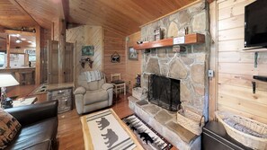 Een gezellig interieur van een chalet met een stenen openhaard, houten wanden, een comfortabele fauteuil en een aan de muur bevestigde televisie.