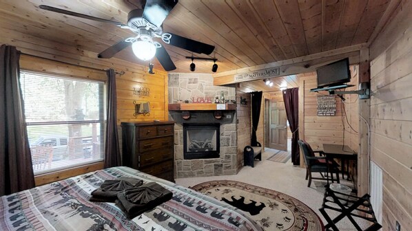Een knus, chalet-achtig vertrek met een bed, een open haard, een plafondventilator en een stenen muur.