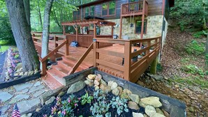 Une cabane dotée d’une terrasse en bois, de murs en pierre et d’un chemin en pierre menant à l’entrée.